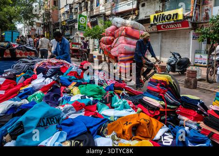 Street market at Chandni Chowk, Old Delhi. A man cycles a rickshaw laden with sacks past stalls of colourful clothes. Stock Photo