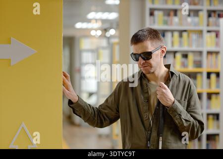 Young Adult Man Navigating Library Using Cane While Blind Stock Photo