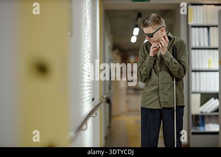 Young Man Using Cane Navigating Library as Blind Individual Stock Photo
