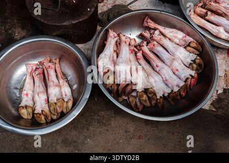 Metal bowls filled with raw animal trotters sit on the ground next to a wooden chopping block at a butcher's stall in Old Delhi. Stock Photo