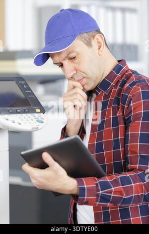technician using a tablet to fix a printer Stock Photo