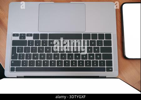 Overhead view of a laptop keyboard and smartphone with blank screen on a wooden desk. Clean, modern workspace composition ideal for business, technolo Stock Photo
