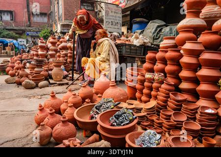 Two women sit amongst a large display of traditional clay pottery and terracotta masks at a market in New Delhi, with buildings in the distance. Stock Photo