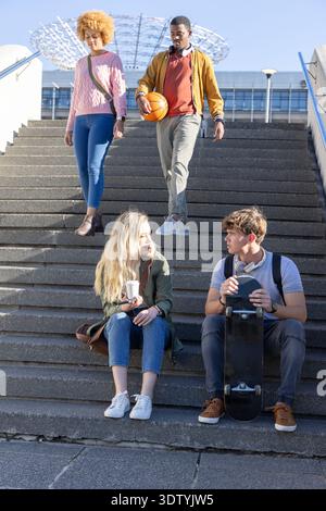 Diverse college students sitting and walking on campus steps holding skateboard, basketball, coffee Stock Photo