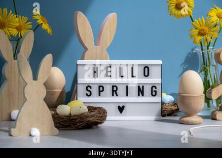 Lightbox with message HELLO SPRING on festive blue background and eco-friendly zero waste natural decoration. Yellow daisies flowers. Bunny egg. Holiday greeting card Stock Photo