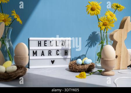 HELLO MARCH text on Lightbox with bunny wooden figures and fresh flowers. Easter composition content still life. Christian symbols of spring holiday  Stock Photo