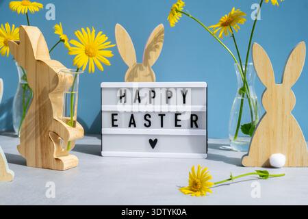 Lightbox with message HAPPY EASTER on festive blue background and eco-friendly zero waste natural decoration. Yellow daisies flowers. Holiday greeting card Stock Photo