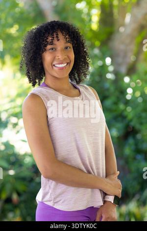 Adult African woman smiling in garden wearing pink top and leggings showing smartwatch sports bra Stock Photo