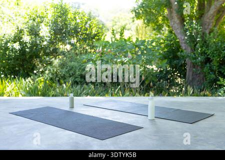 Two gray yoga mats are lying on patio with white water bottles near tops, overlooking garden Stock Photo