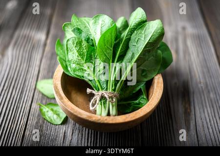 Organic spinach leaves in wooden bowl on textured wooden table. Natural food styling, clean diet and fresh produce concept Stock Photo