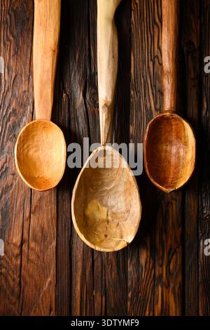 Set of wooden handcraft spoons displayed vertically on dark wooden boards. Cooking accessories, rustic kitchenware, natural wood grain, culinary concept Stock Photo