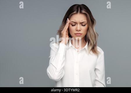 Frustrated young businesswoman suffering from headache or migraine tough hurting temple to relief pain. Tired business lady or office worker in white shirt feeling bad from stress at work or overwork || Model released Stock Photo
