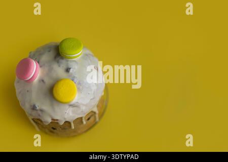 Top view of Easter cake with glossy icing drips and colorful macarons on yellow background, creative spring flat lay composition Stock Photo