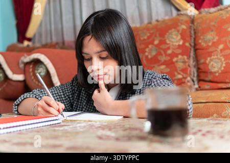 Portrait of a young Indonesian woman focusing on her smartphone and writing notes. Stock Photo