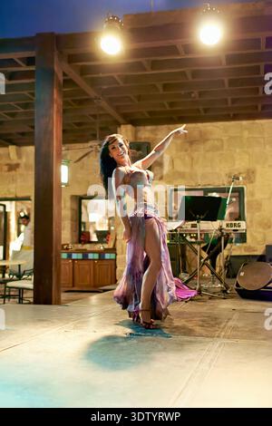A dancer performs belly dance on stage in Jordan. The venue has lights and an audience enjoying the show. Stock Photo