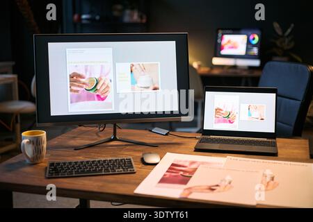 Modern workspace showing desktop monitor and laptop displaying skincare product design, digital tablet and keyboard on wooden desk, printed marketing materials and coffee mug visible Stock Photo