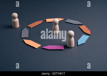 A conceptual studio shot of wooden peg figures and colorful arrows on a dark background, illustrating business concepts of social exclusion, team incl Stock Photo