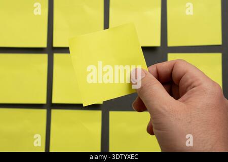 Hand holding one blank sticky note taken from a grid, symbolizing selection, focus, planning and organization. Stock Photo