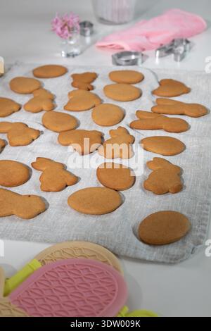 Numerous freshly baked Easter bunny and egg shaped cookies are arranged on a light linen cloth in a kitchen. Stock Photo