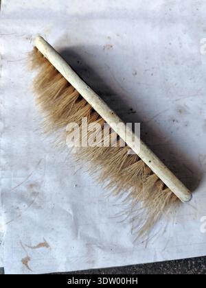 Old hand brush with light bristles and worn handle lying on a dirty white surface. Used cleaning brush with visible stains, scratches, and rough textu Stock Photo