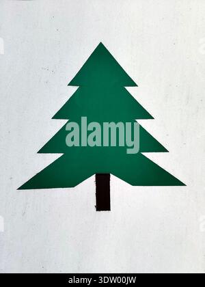 Green geometric tree symbol painted on a white wall. Flat shape with triangular sections and black trunk, visible wall texture, small cracks, scratche Stock Photo