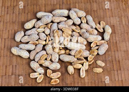 A scattered collection of whole peanuts and shelled kernels arranged on a woven bamboo mat, showcasing their natural texture and color. Stock Photo