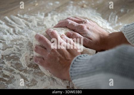 Young woman kneading bread dough on wooden table in a home kitchen. Stock Photo