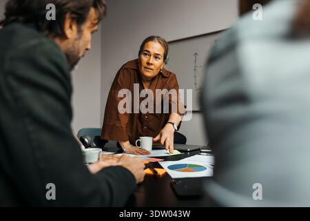 Mature businesswoman discussing over documents with colleagues in meeting at office Stock Photo
