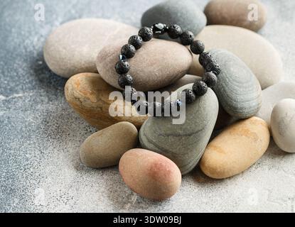 Beautiful bracelet made of natural black volcanic lava. Jewelry made of round-shaped beads is placed on large sea stones. Selective focus,  copy space Stock Photo