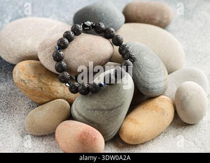 Beautiful bracelet made of natural black volcanic lava. Jewelry made of round-shaped beads is placed on large sea stones. Selective focus Stock Photo