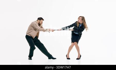 Businessman and businesswoman in formal outfits playfully pulling against each other in studio. Stock Photo