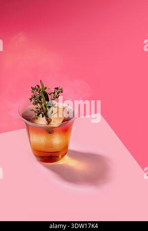 Smoked Old Fashioned Cocktail with Large Ice Cube and Fresh Rosemary Thyme Garnish Stock Photo