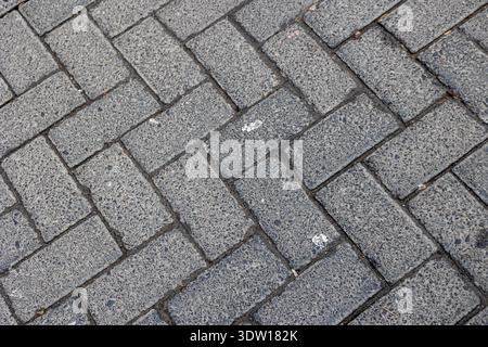 Gray textured interlocking brick pavers forming a classic herringbone pattern, creating a durable and decorative surface for pathways, sidewalks, and Stock Photo