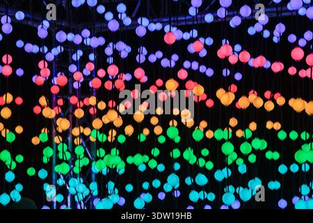Abstract background of hanging glowing LED spheres in a dark room, creating colorful bokeh lights in rainbow rows; modern immersive light installation Stock Photo