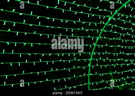 Green LED string lights forming curved lines on a dark background, creating an abstract festive pattern with a tunnel-like arc. Stock Photo