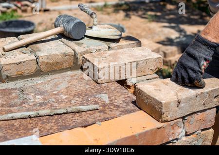 Bricklayer in a work glove laying bricks with mortar on a construction site. house building, manual labor, professional service. Stock Photo