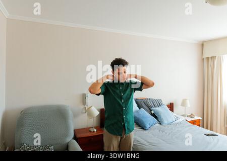 Young man adjusting shirt collar in modern bedroom Stock Photo