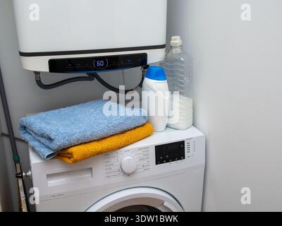 Laundry area in a home interior with washing machine, clean folded towels on top, and bottles of detergent and fabric softener. Concept of housekeepin Stock Photo