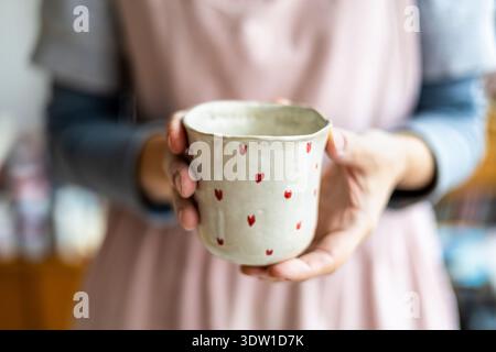 Woman's hands holding a handmade mug with a heart-shaped pattern Stock Photo