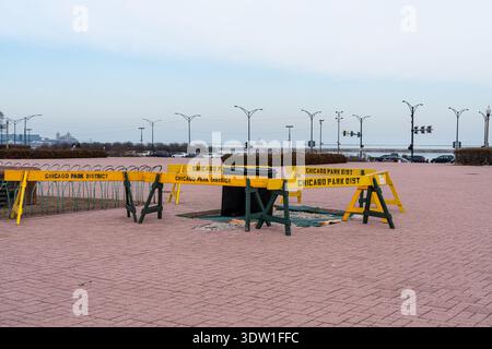 Chicago Park District brick pavement repair in a public park, fenced with bright yellow safety barriers and trash bins nearby. Quiet urban maintenance Stock Photo