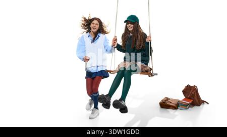 Teen girls smiling on swing with school bags isolated on white. Stock Photo