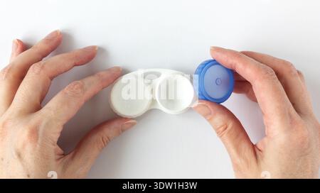 Woman's hand removes the blue lid of a contact lens case. Empty white plastic lens case with compartments for storing contact lenses on a white backgr Stock Photo