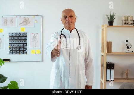 senior doctor in white coat holding hand for handshake at camera. Webcam head shot. counseling patient during visit to clinic Stock Photo