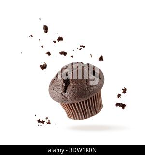 Fresh baked single chocolate muffin with crumbs flying on white background. Sweet dark cupcake falling. Pastry card with copy space Stock Photo