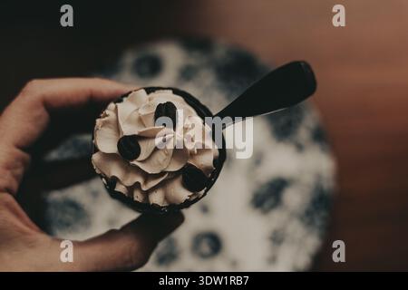 Delicious coffee dessert with whipped cream and coffee beans in a dark chocolate cup. A hand holds a small cup of coffee-flavored dessert Stock Photo