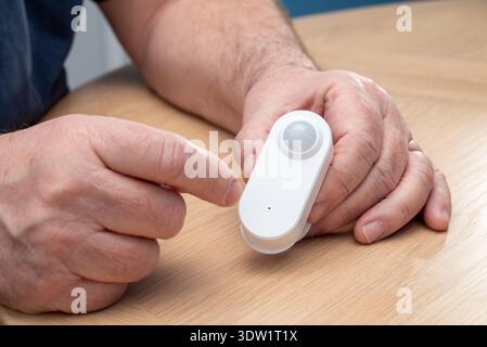 A person is holding a white motion sensor, likely for a smart home security system, about to reset it. Stock Photo