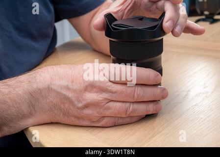 A person's hands are shown placing a lens hood on a camera lens, likely for protection or storage. Stock Photo