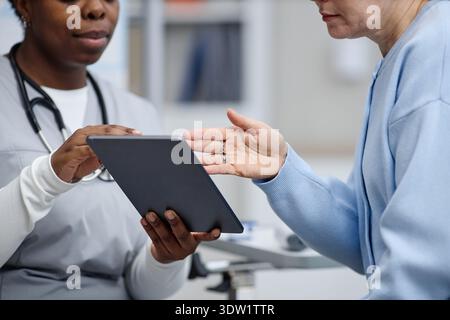 Middle Aged Caucasian Woman Consulting Black Female Nurse Using Digital Tablet Stock Photo