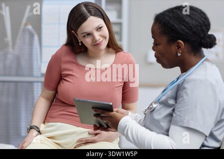 Caucasian Young Adult Woman Consulting Black Female Doctor Using Digital Tablet Stock Photo