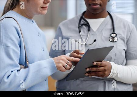 Middle Aged Caucasian Woman Interacting with Black Female Nurse Using Tablet Stock Photo